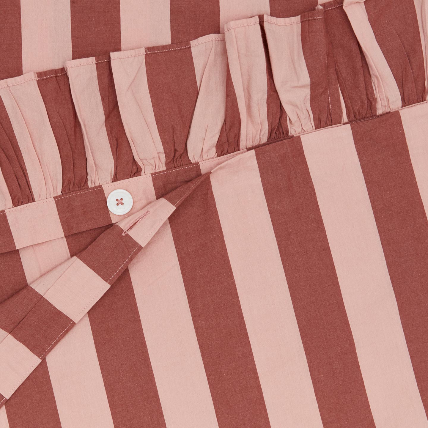 Detailed view of folded blush and terracotta striped ruffled duvet cover
